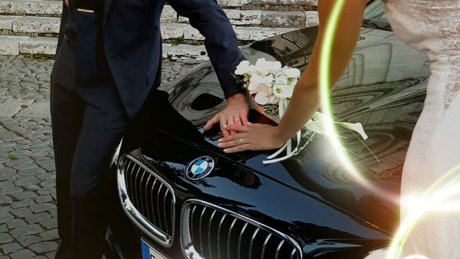 Due sposi mostrano le loro fedi nuziali mentre appoggiano la mano sul cofano di una BMW della Roman Limousine Service